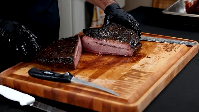 A person slicing a perfectly smoked brisket on a wooden cutting board