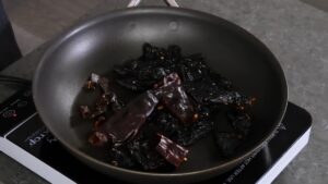 Dried chilies are being toasted in a skillet on a stovetop to enhance their flavor before blending