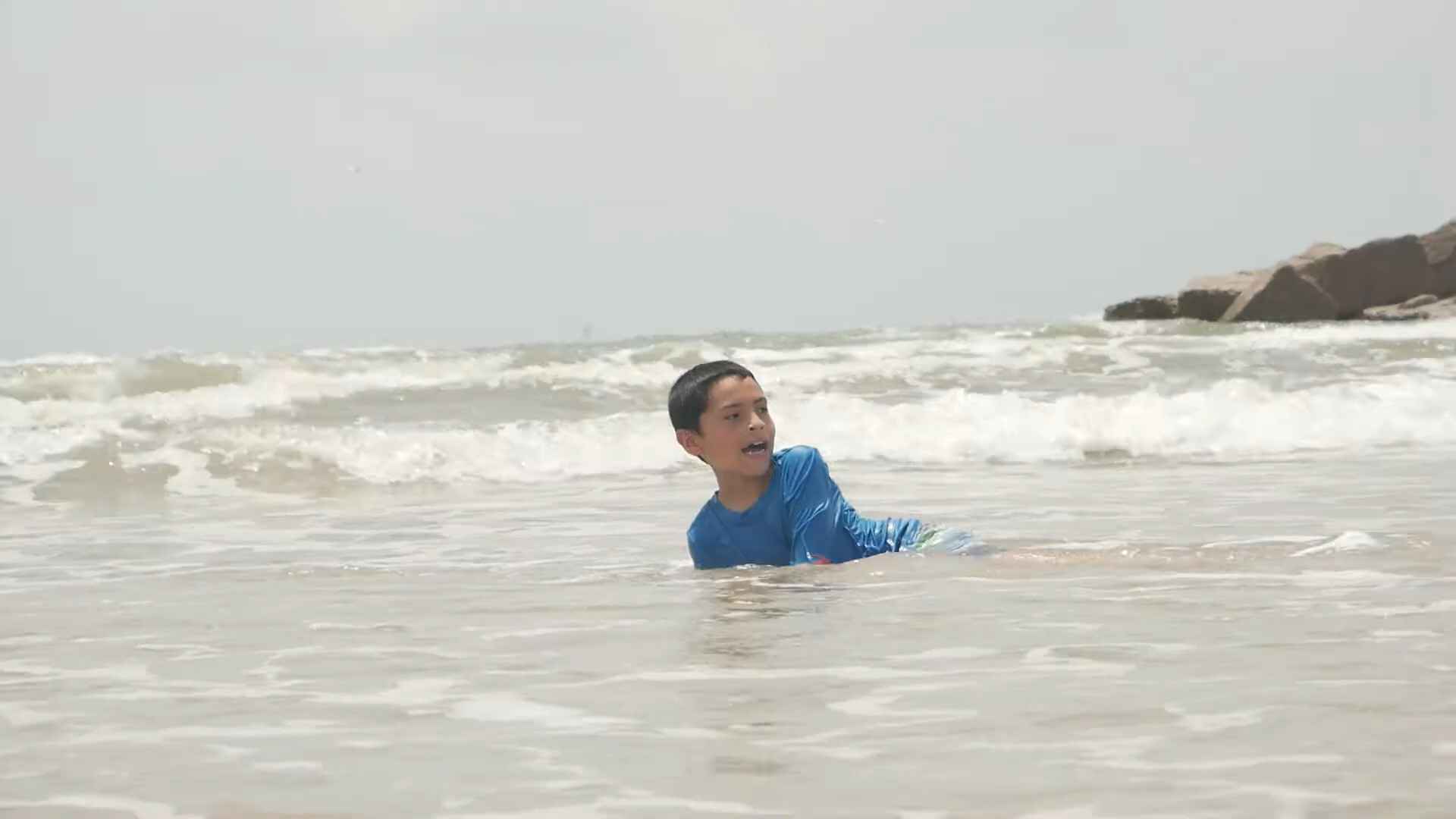 Young boy in a blue rash guard playing in the shallow waves at Mustang Island State Park beach in Texas