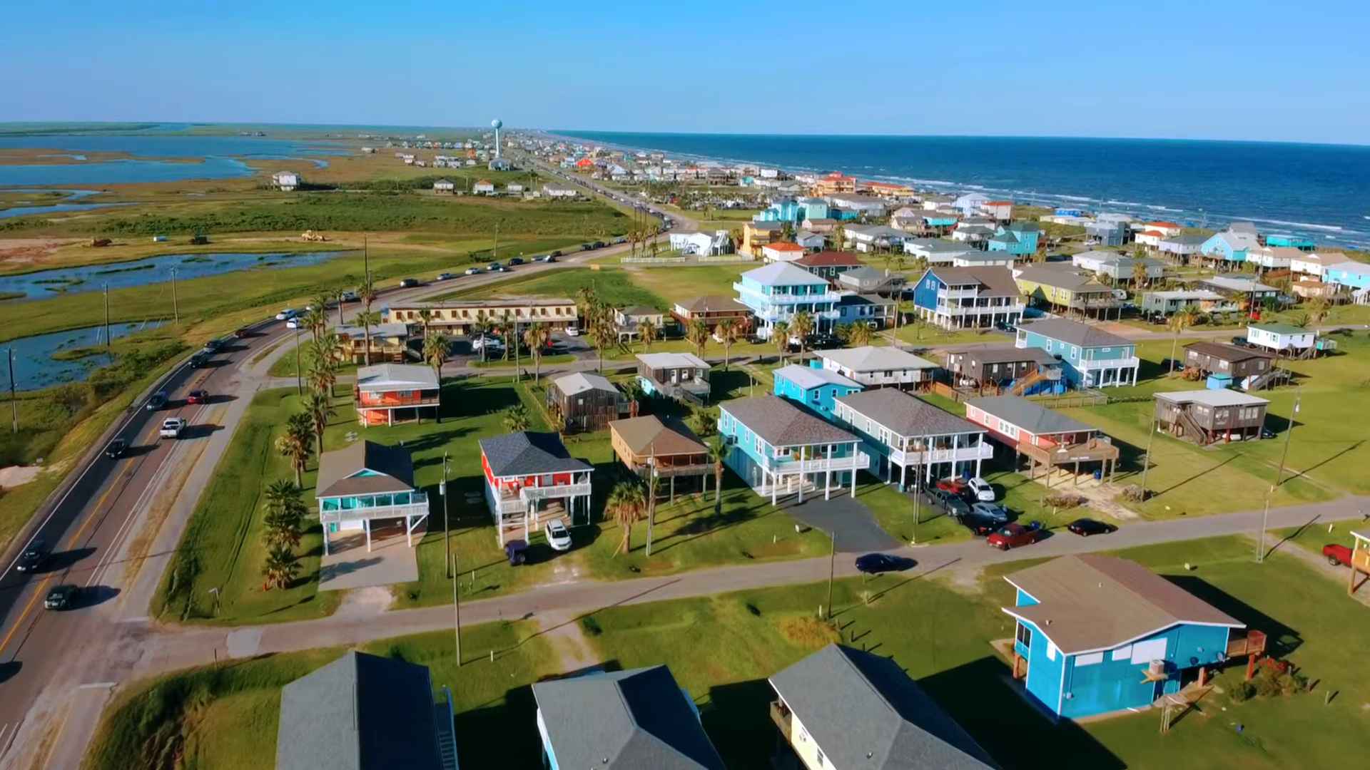 Aerial view of Surfside Beach, Texas, showing colorful stilted beach houses near the ocean and coastal wetlands
