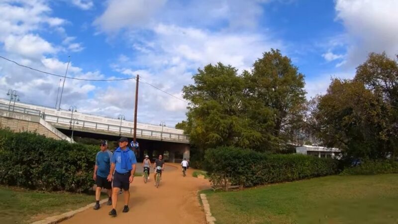 Visitors walking and biking on a multi-use trail near Lake Austin with a bridge in the background